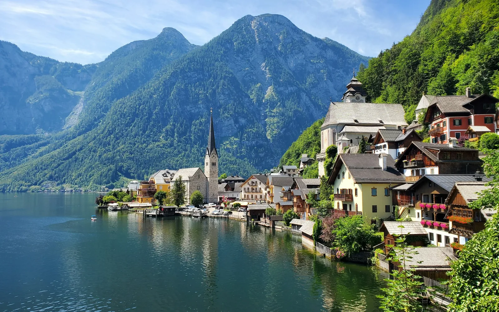Pastel lakeside houses and a church spire below alpine mountains reflected in Lake Hallstatt